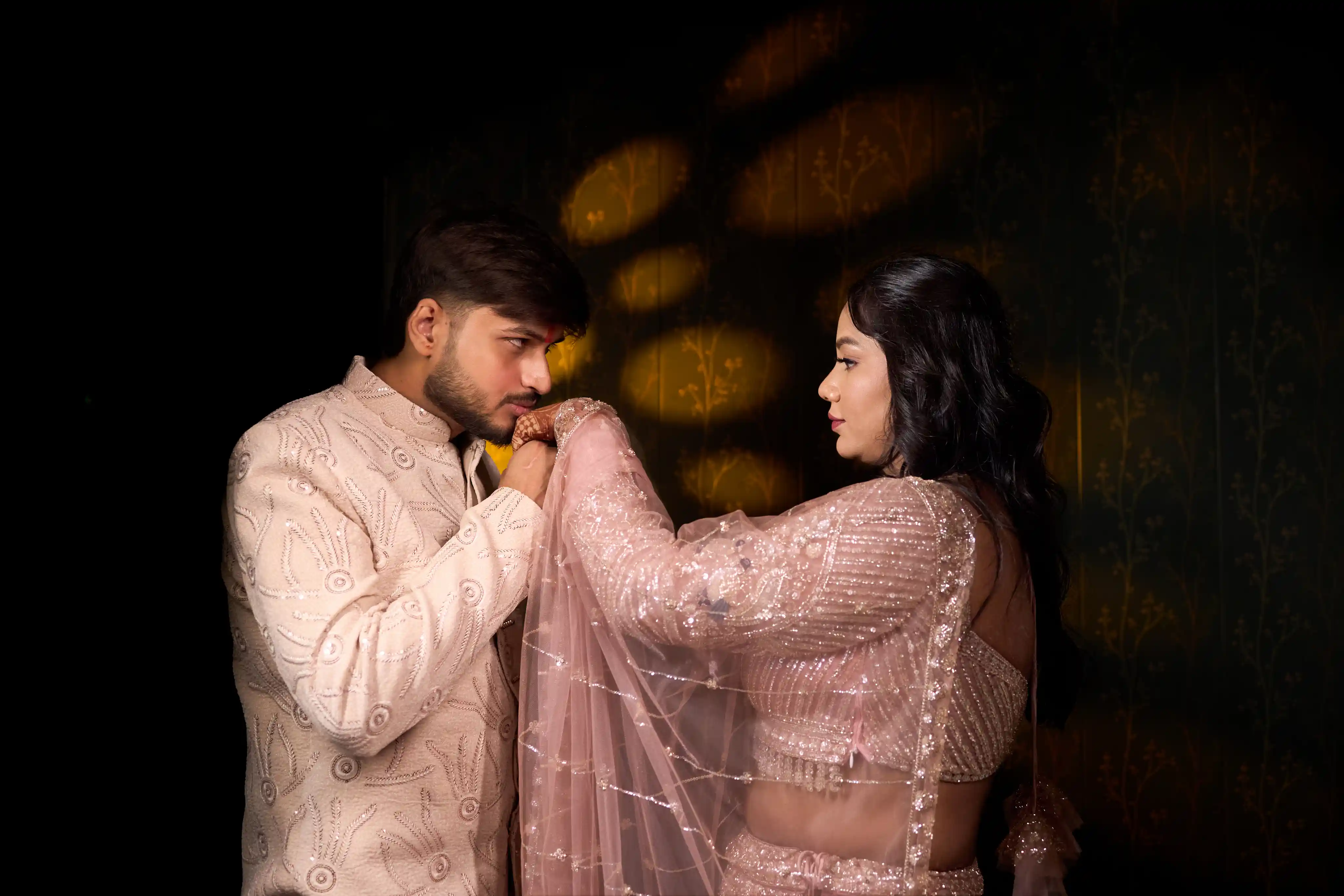 Engagement pose idea: groom kissing the bride's hand against patterned light, Varanasi, by The WeddingShoot